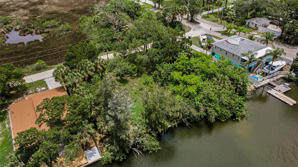 An aerial view shows a vacant, tree-covered waterfront lot situated between two residential properties — Lot 15 RICE ROAD, HUDSON, FL