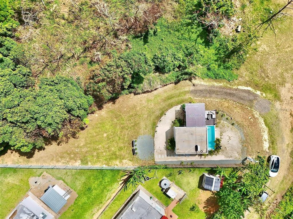 An aerial view shows a house with a swimming pool, gravel driveway, and surrounding greenery — Lot 1 KM. 8.0 INT. CRUZ WARD, MOCA, PR