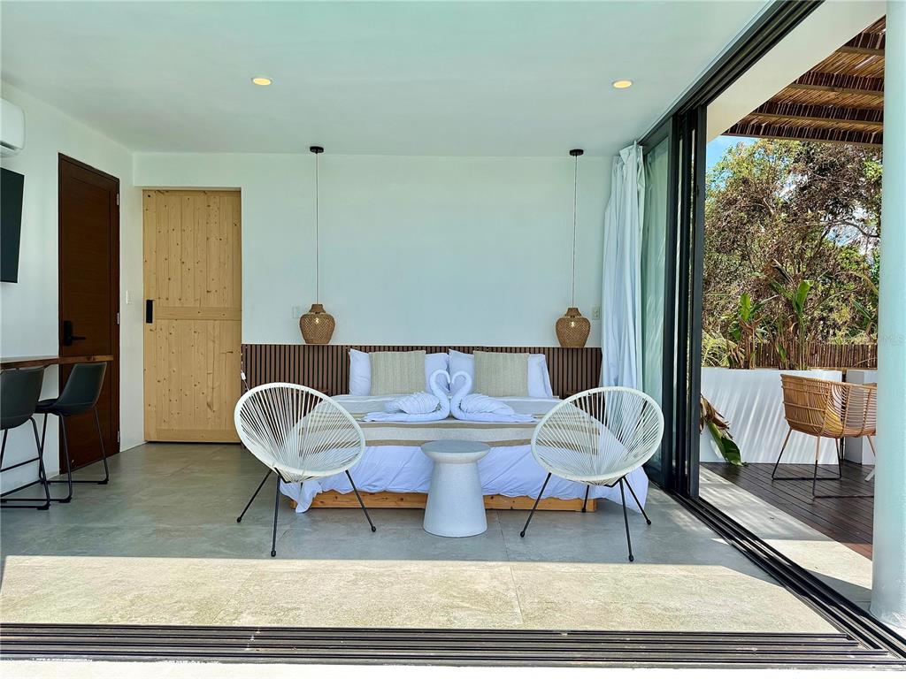 A modern bedroom features a bed with towel swans, two white chairs, and sliding glass doors — Lot 1 KM. 8.0 INT. CRUZ WARD, MOCA, PR