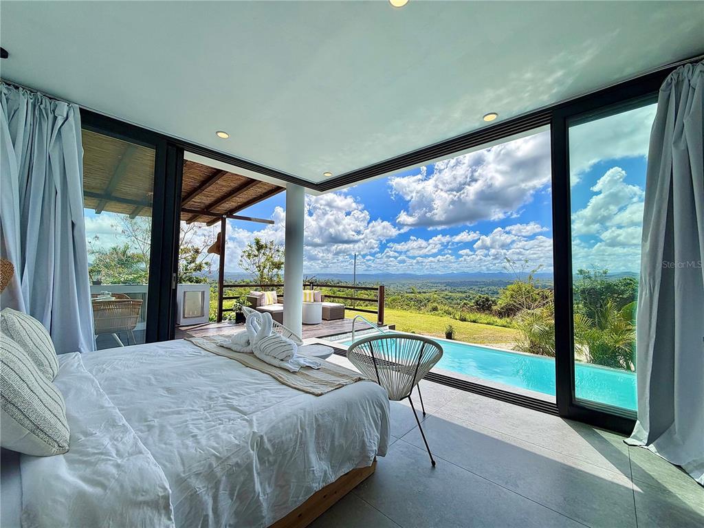A bedroom with floor-to-ceiling windows overlooks a private pool and a scenic landscape — Lot 1 KM. 8.0 INT. CRUZ WARD, MOCA, PR