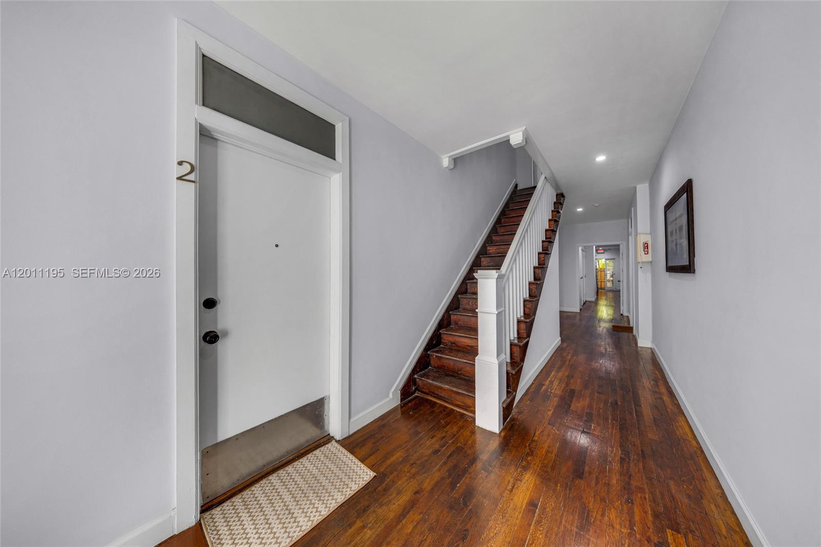 An indoor hallway features hardwood floors, a white door labeled two, and a wooden staircase — 1610 Salzedo St, Coral Gables FL 33134, CORAL GABLES, FL