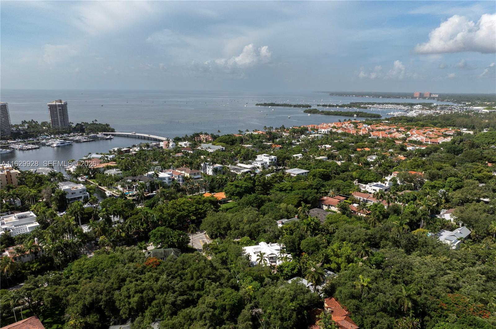 An aerial view shows a coastal neighborhood with dense trees, residential homes, and a marina — 1701 S Bayshore Drive, Miami FL 33133, MIAMI, FL