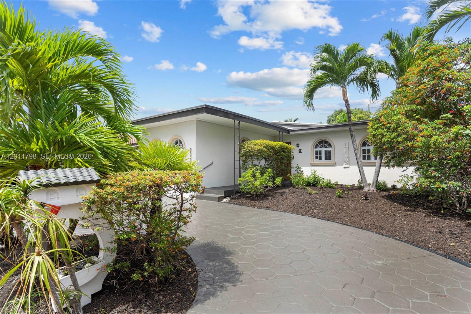 A single-story house with a paved driveway, arched windows, and palm trees in the yard — 6921 Trouville Esplanade, Miami Beach FL 33141, MIAMI BEACH, FL