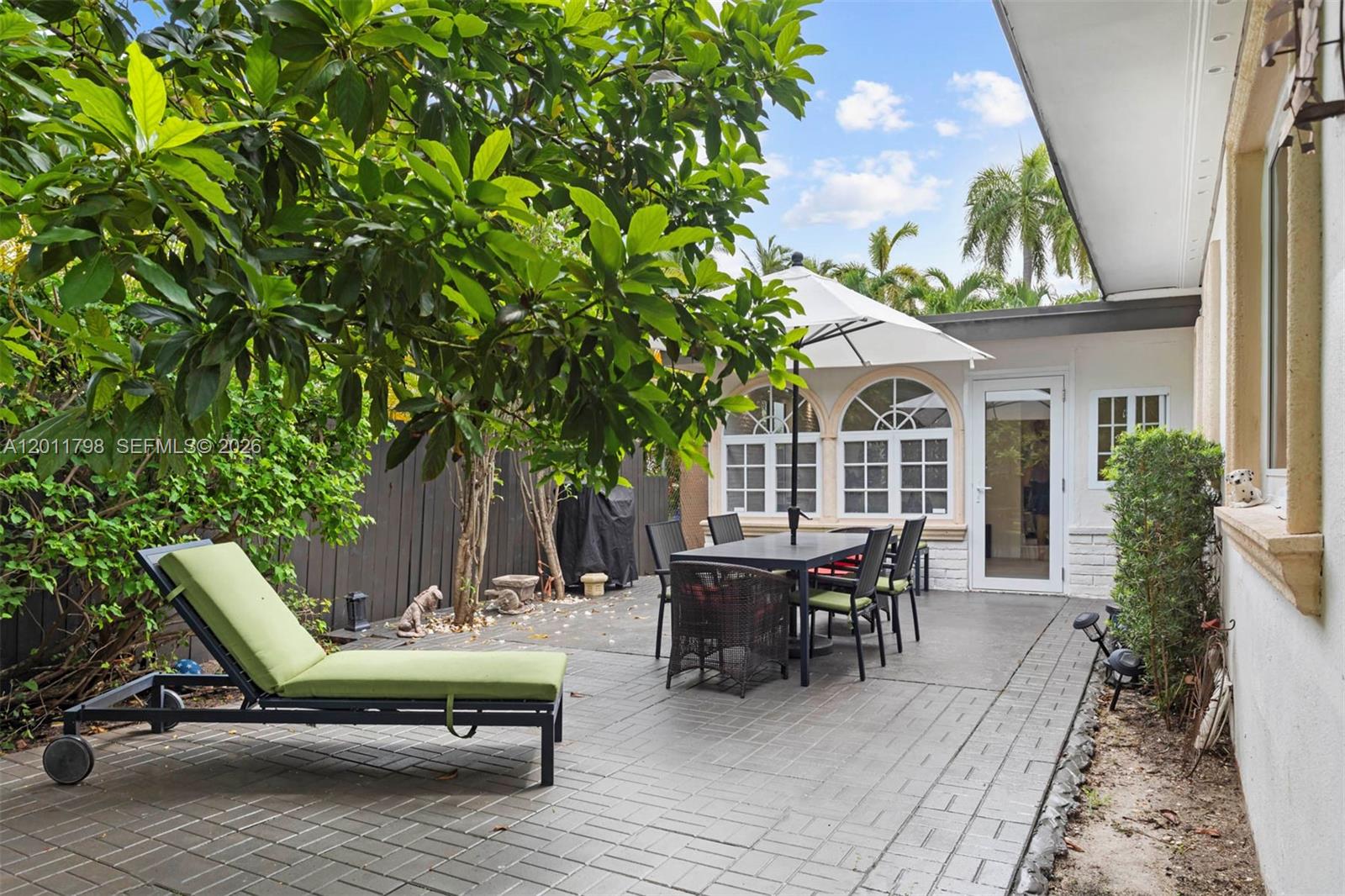 A paved patio features a dining set with an umbrella, a lounge chair, and landscaping — 6921 Trouville Esplanade, Miami Beach FL 33141, MIAMI BEACH, FL