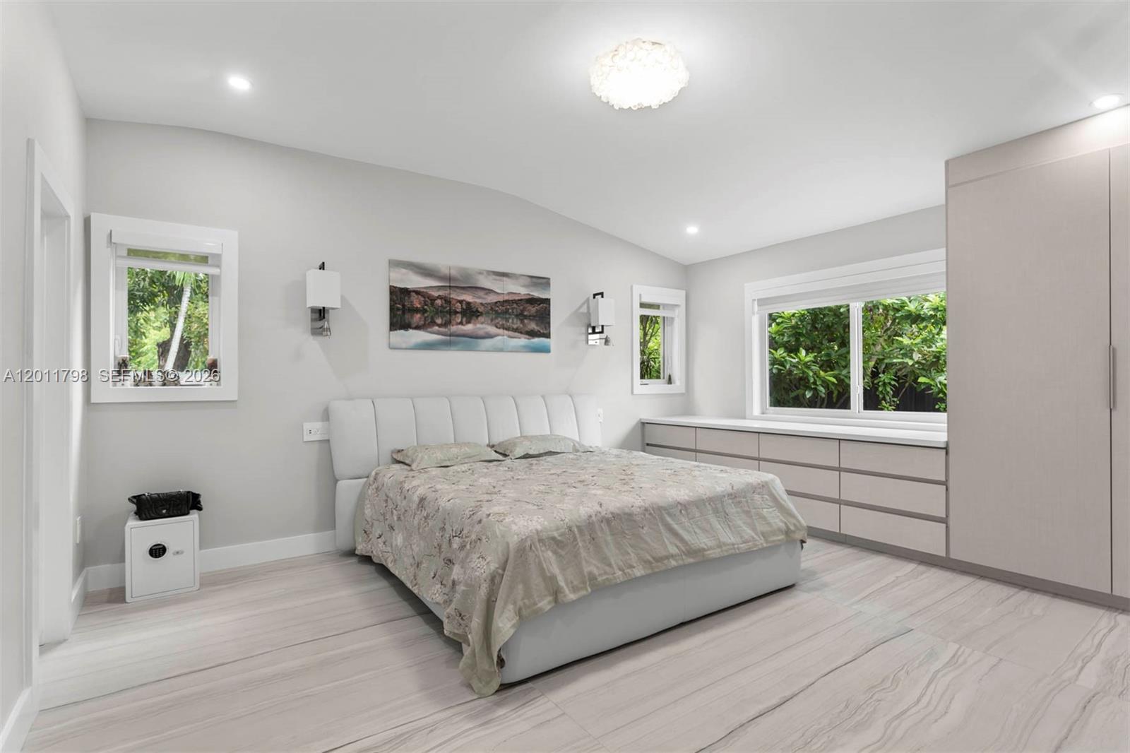 A bedroom features a white bed, built-in storage, light wood-look flooring, and two windows — 6921 Trouville Esplanade, Miami Beach FL 33141, MIAMI BEACH, FL