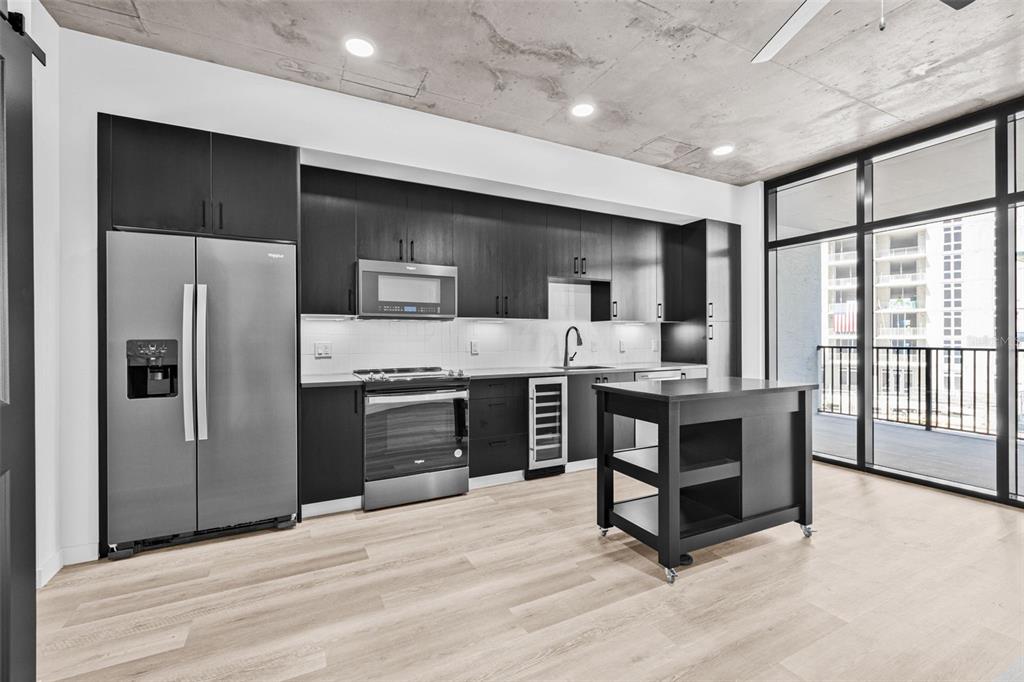 A modern kitchen features dark cabinetry, stainless steel appliances, a rolling island, and concrete ceilings — 221 MAIN STREET N UNIT A1-1004, ST PETERSBURG, FL