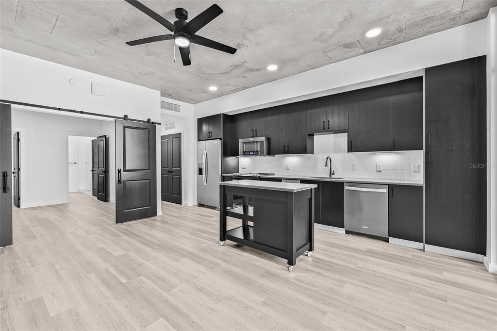 A modern kitchen features dark cabinetry, a movable island, and an exposed concrete ceiling — 221 MAIN STREET N UNIT A1-1004, ST PETERSBURG, FL