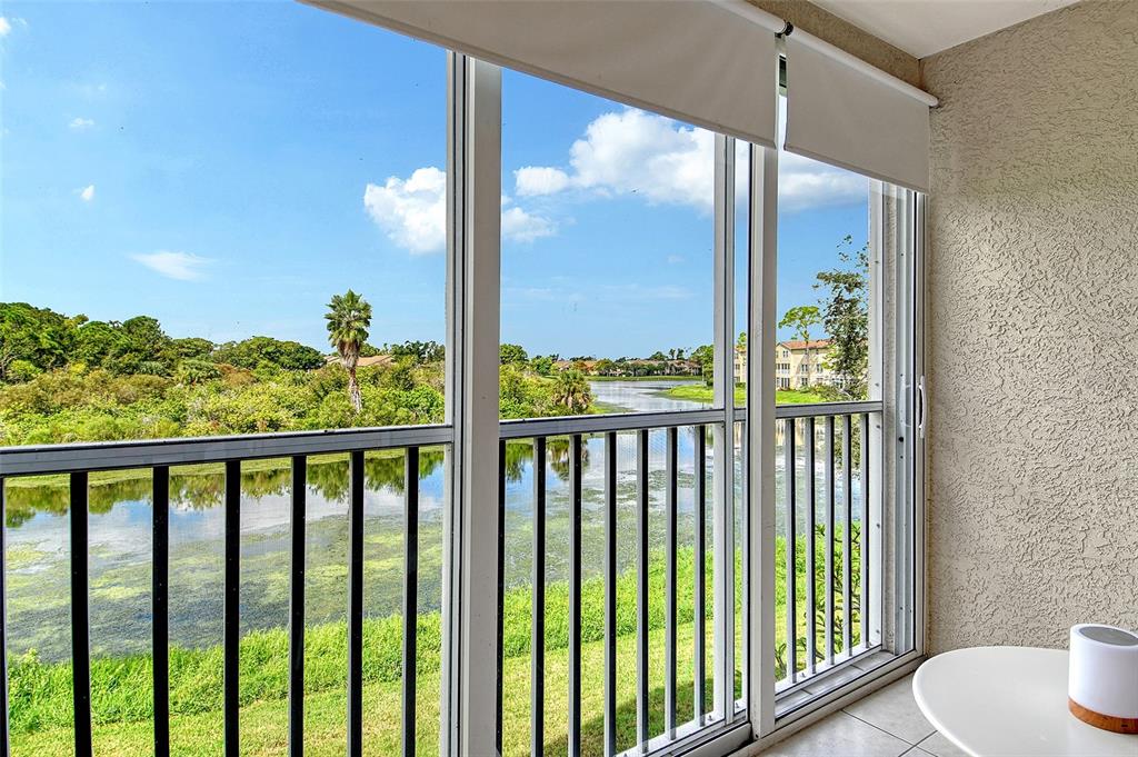 A screened-in balcony overlooks a lake surrounded by lush green trees and residential buildings — 8370 WINGATE DRIVE UNIT 724, SARASOTA, FL