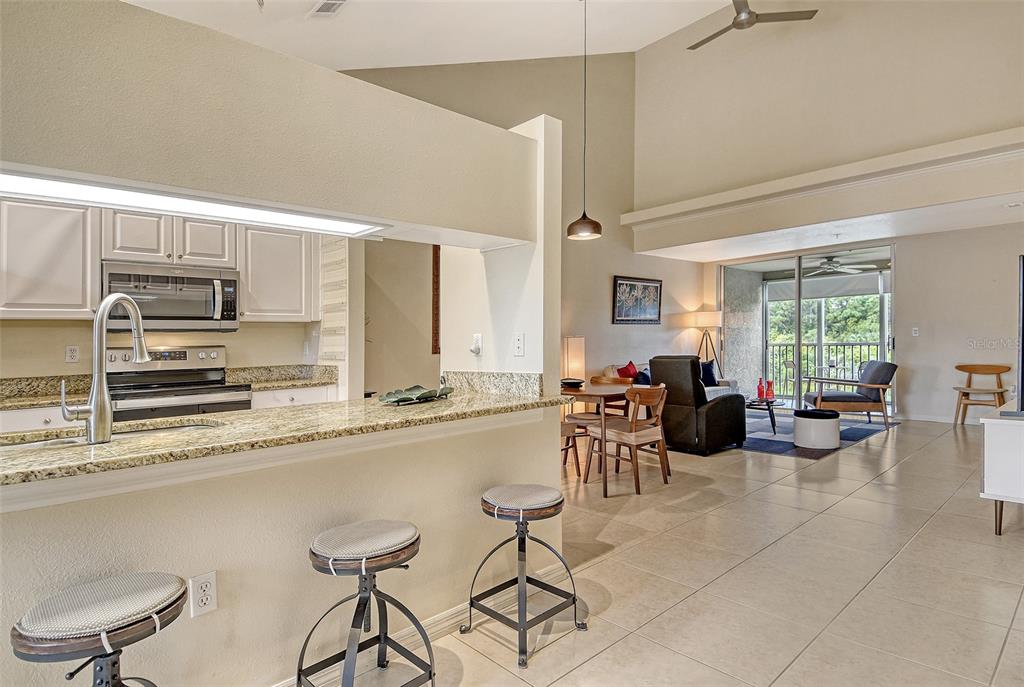 A kitchen with granite countertops and bar seating overlooks an open-concept living area with balcony — 8370 WINGATE DRIVE UNIT 724, SARASOTA, FL