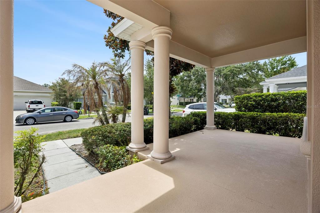 A covered front porch with beige concrete flooring and two white columns overlooks a street — 8662 ABBOTSBURY DRIVE, WINDERMERE, FL
