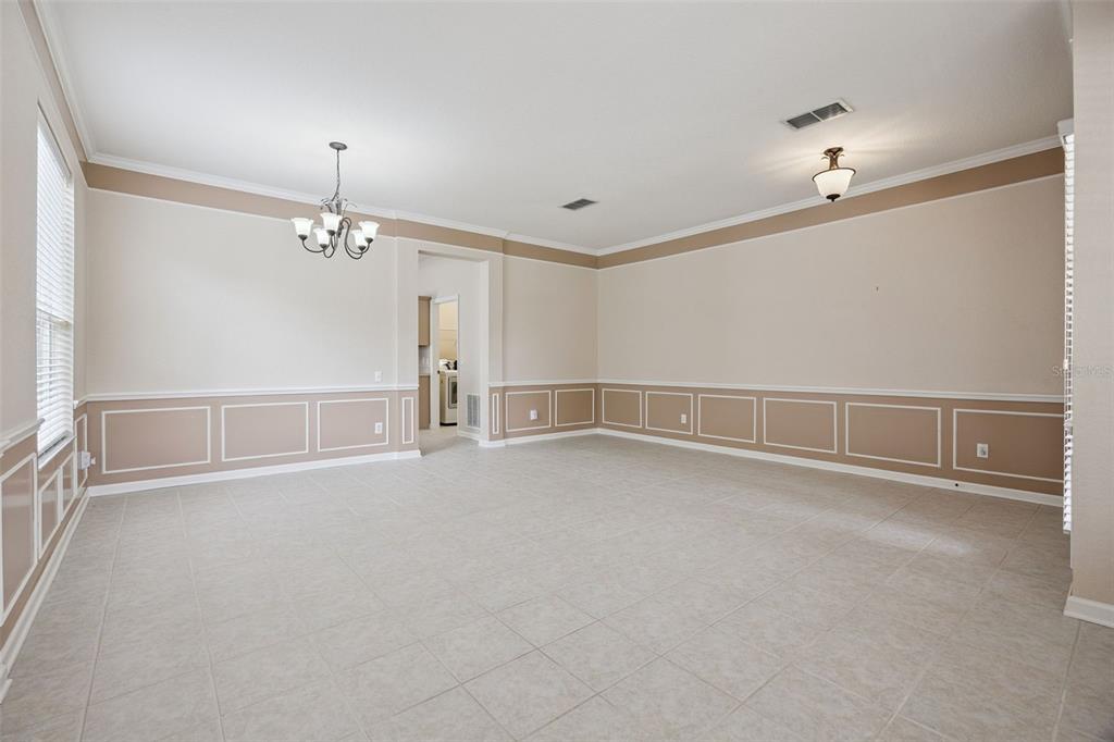 An empty room features tile flooring, wainscoting, a chandelier, and a doorway to a kitchen — 8662 ABBOTSBURY DRIVE, WINDERMERE, FL