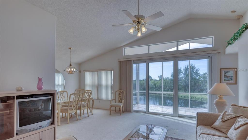 A living and dining area features vaulted ceilings, a ceiling fan, and sliding glass doors — 718 LIGHTHOUSE DRIVE, TARPON SPRINGS, FL