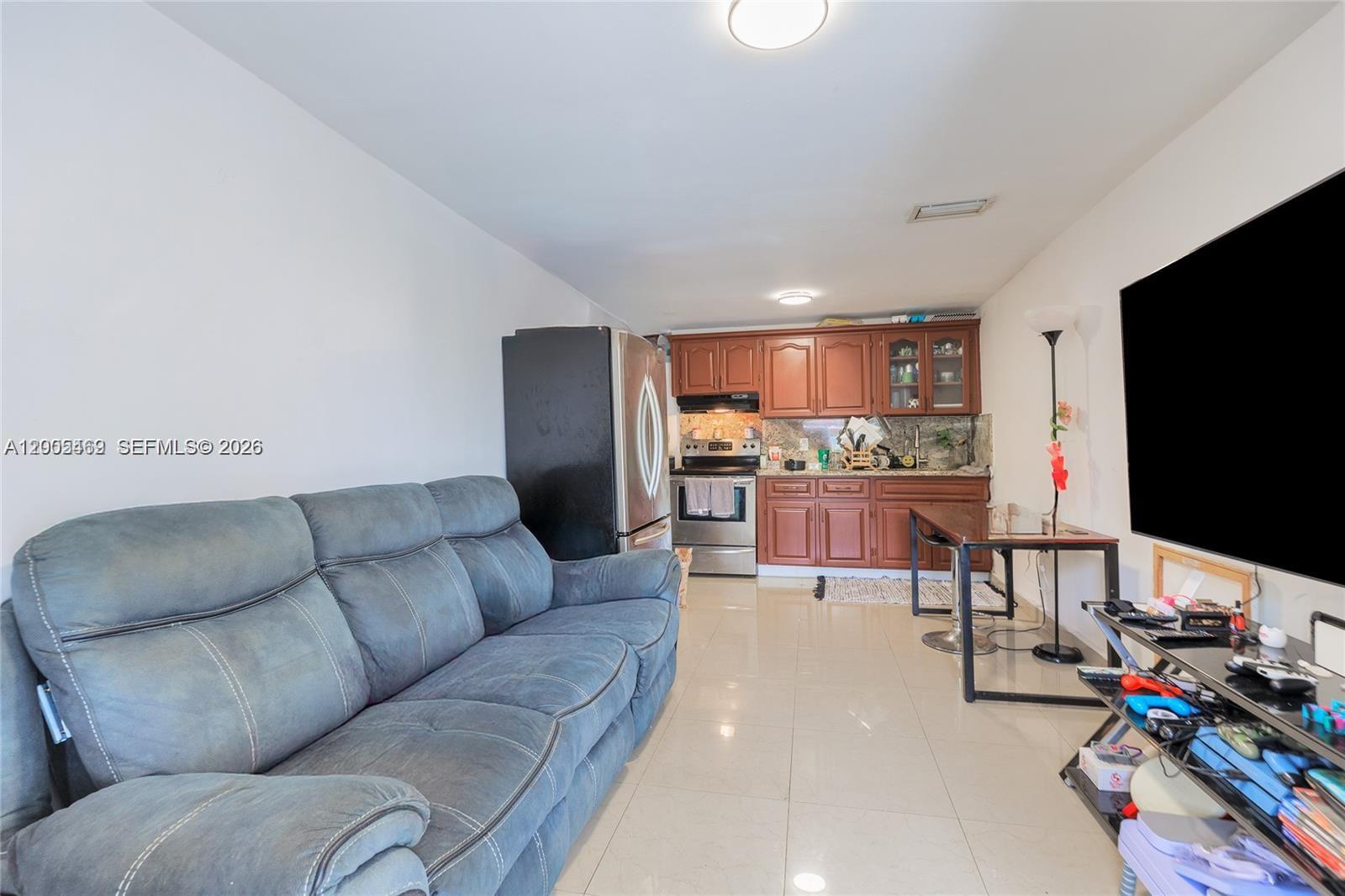 A living room with a grey sofa, a wall-mounted television, and an adjacent kitchen — 14601 NW 10th Ave # 2, Miami FL 33168, MIAMI, FL