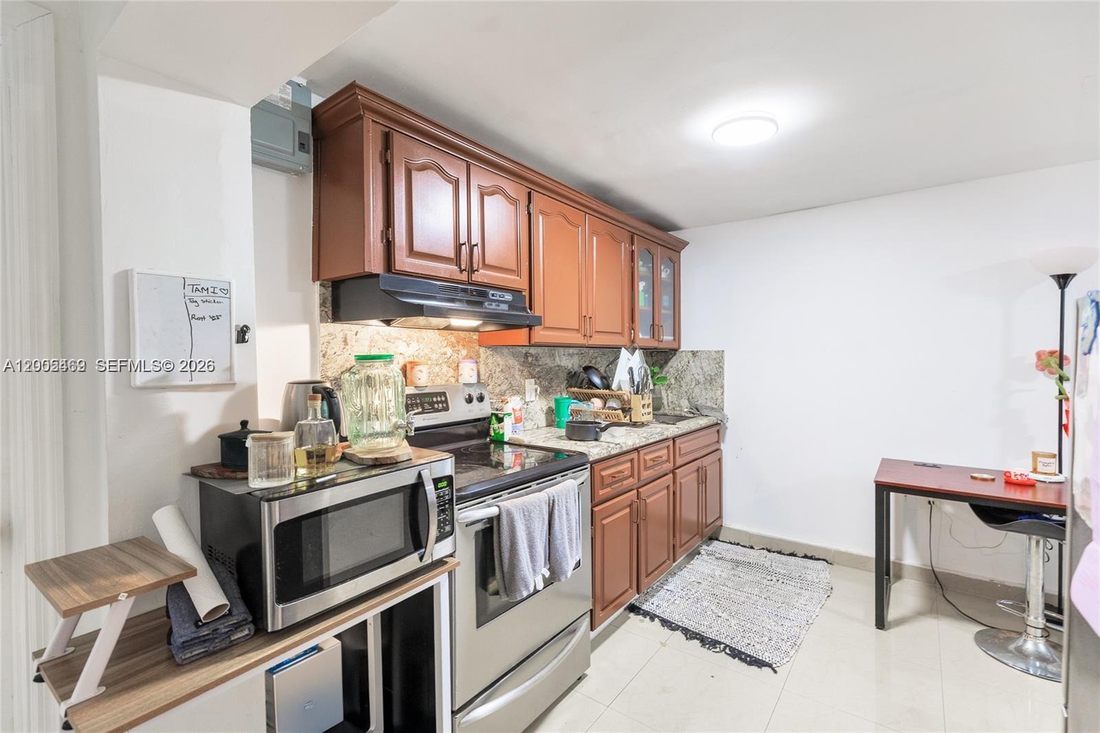 A kitchen features wooden cabinets, stainless steel appliances, granite countertops, and a small dining table — 14601 NW 10th Ave # 2, Miami FL 33168, MIAMI, FL