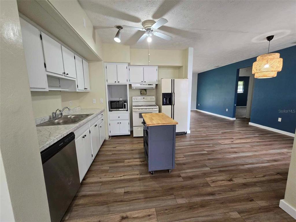 A kitchen with white cabinets, stainless steel appliances, and a wood-topped island opens to a room — 665 SE HERON STREET, KEYSTONE HEIGHTS, FL