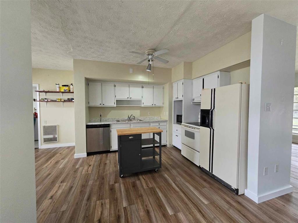 A kitchen features white cabinets, stainless steel appliances, a rolling island, and wood-look flooring — 665 SE HERON STREET, KEYSTONE HEIGHTS, FL