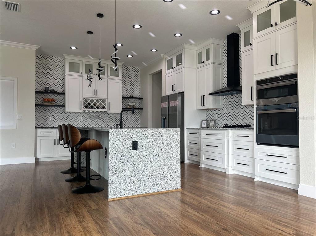 A foyer features wood-look flooring, white columns, and a modern geometric chandelier — 1126 ARREDONDO STREET, NORTH PORT, FL