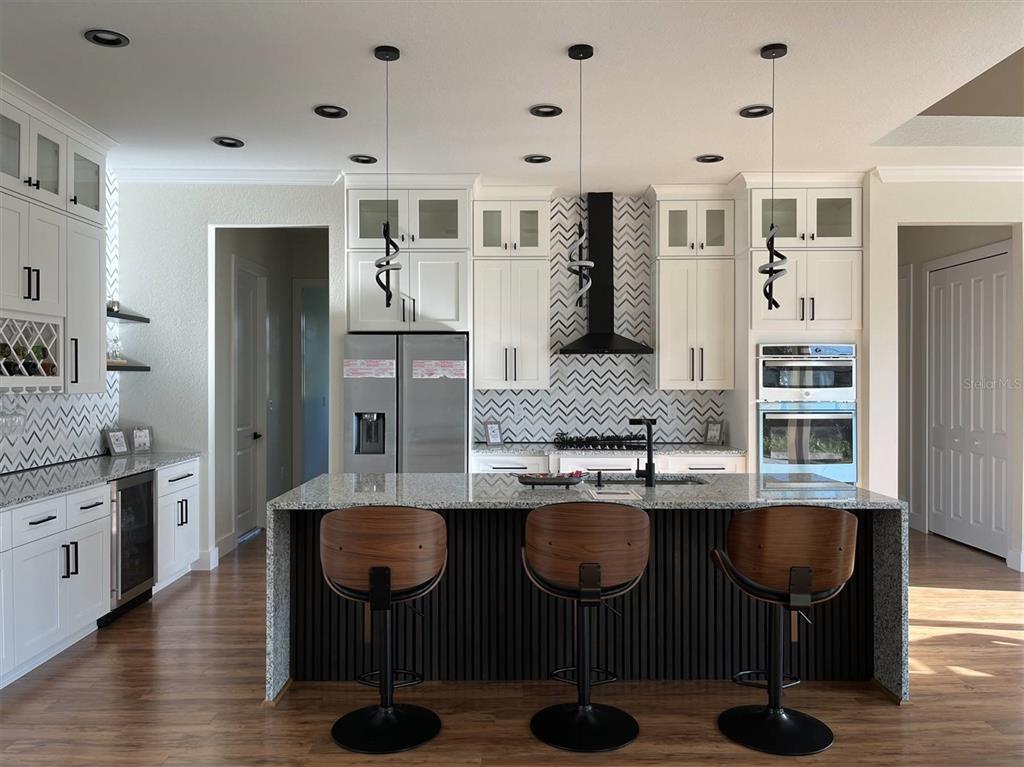 A modern kitchen features white cabinetry, a granite-topped island, chevron-patterned backsplash, and stainless steel appliances — 1126 ARREDONDO STREET, NORTH PORT, FL