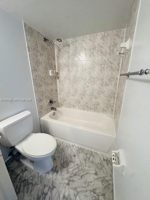 A bathroom features a white toilet, a bathtub with a showerhead, and marble-patterned tile — NORTH MIAMI, FL