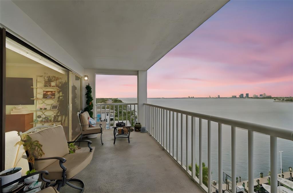 A balcony with patio furniture overlooks a calm bay under a pink sunset sky — 2 ADALIA AVENUE UNIT 704, TAMPA, FL