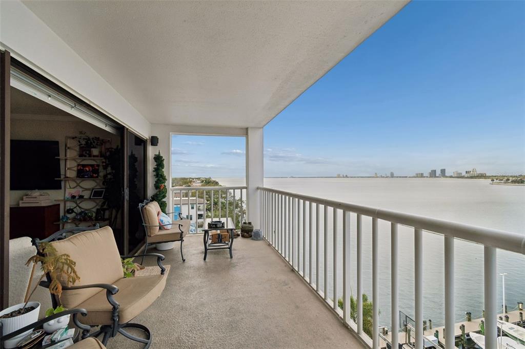 A covered balcony with outdoor seating overlooks a large body of water and distant buildings — 2 ADALIA AVENUE UNIT 704, TAMPA, FL