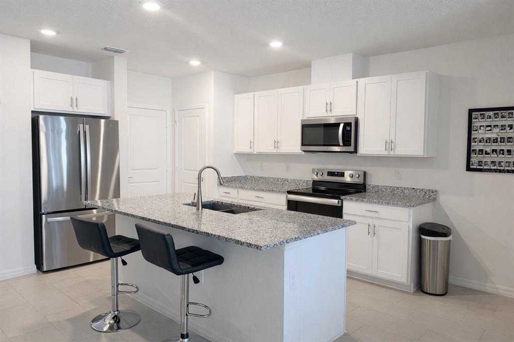 A kitchen with white cabinets, granite countertops, stainless steel appliances, and a central island — 1536 MIRABELLA CIRCLE UNIT 1536, DAVENPORT, FL