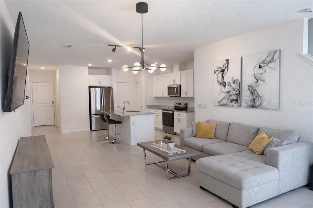 A modern open-concept living room and kitchen featuring white cabinetry, stainless appliances, and tile flooring — 1536 MIRABELLA CIRCLE UNIT 1536, DAVENPORT, FL