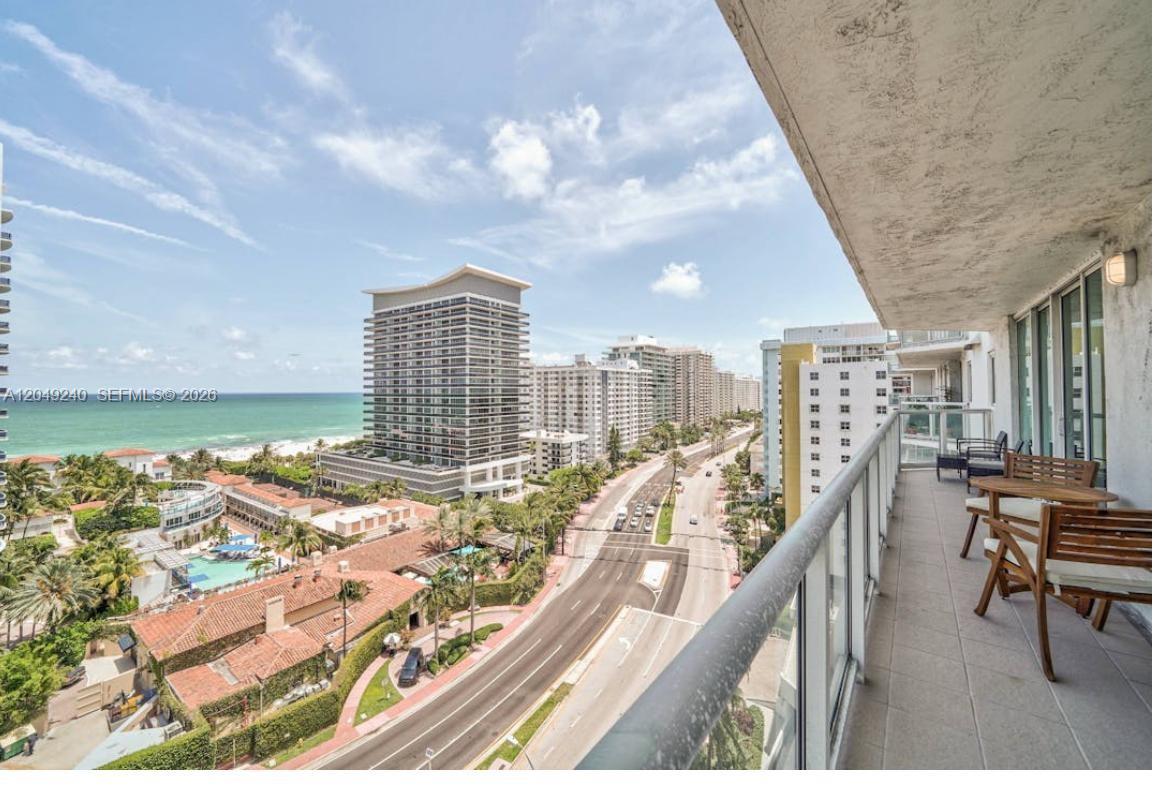 A balcony with outdoor furniture overlooks a coastal city street and the ocean — 5900 Collins Ave # 1406, Miami Beach FL 33140, MIAMI BEACH, FL