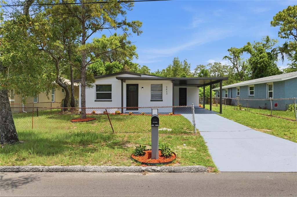 A single-story house with a white exterior, a carport, and a front yard with fencing — 3412 E HENRY AVENUE, TAMPA, FL
