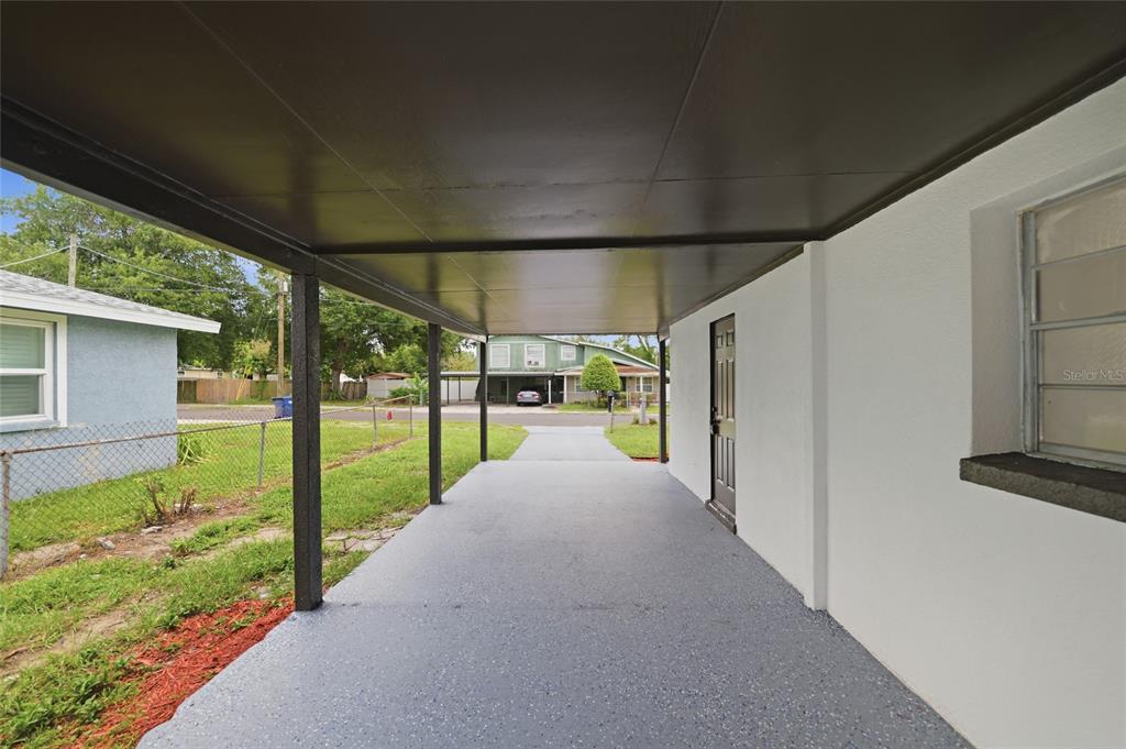 A covered carport with a gray speckled concrete floor and a dark brown ceiling — 3412 E HENRY AVENUE, TAMPA, FL