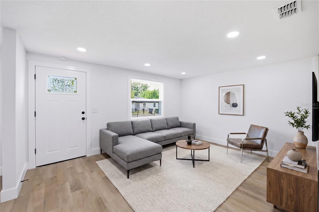 A living room features a grey sectional sofa, a leather chair, and light wood flooring — 3412 E HENRY AVENUE, TAMPA, FL