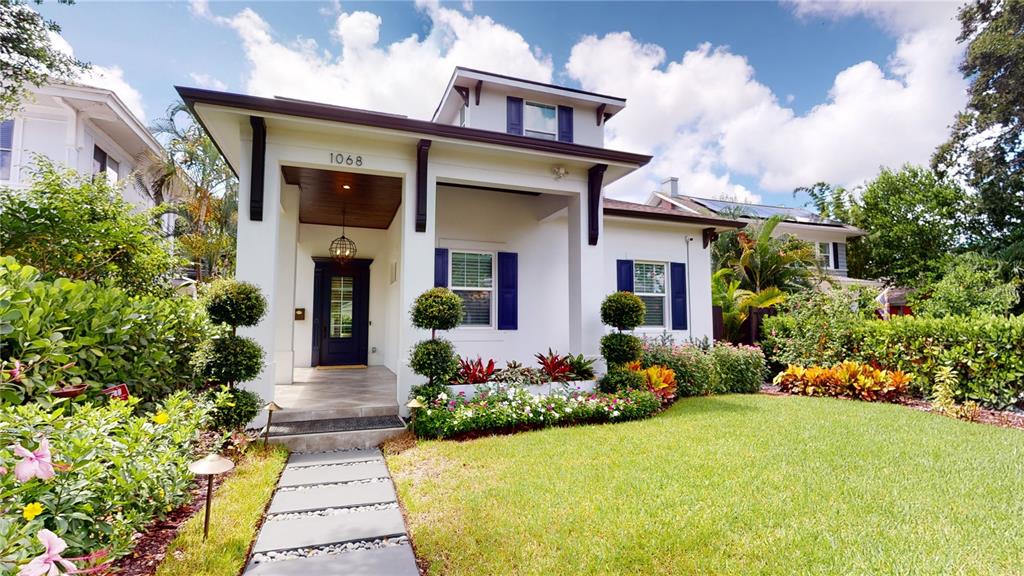 A white house with blue shutters features a covered entryway and a landscaped front yard — 1068 19TH AVENUE N, ST PETERSBURG, FL