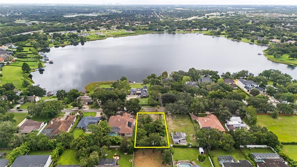 An aerial view shows a vacant, tree-covered lot outlined in yellow near a large lake — 1516 HEMPEL AVENUE, WINDERMERE, FL