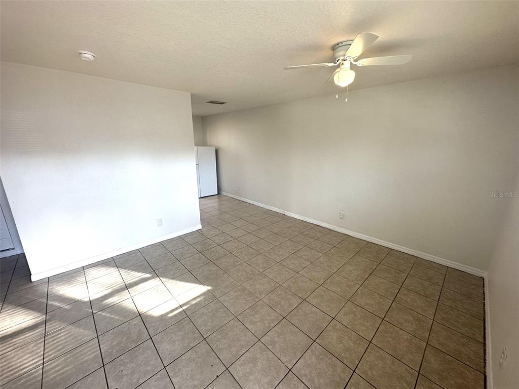 An empty room features light-colored tile flooring, white walls, and a ceiling fan — 9601 N 10TH STREET UNIT B, TAMPA, FL