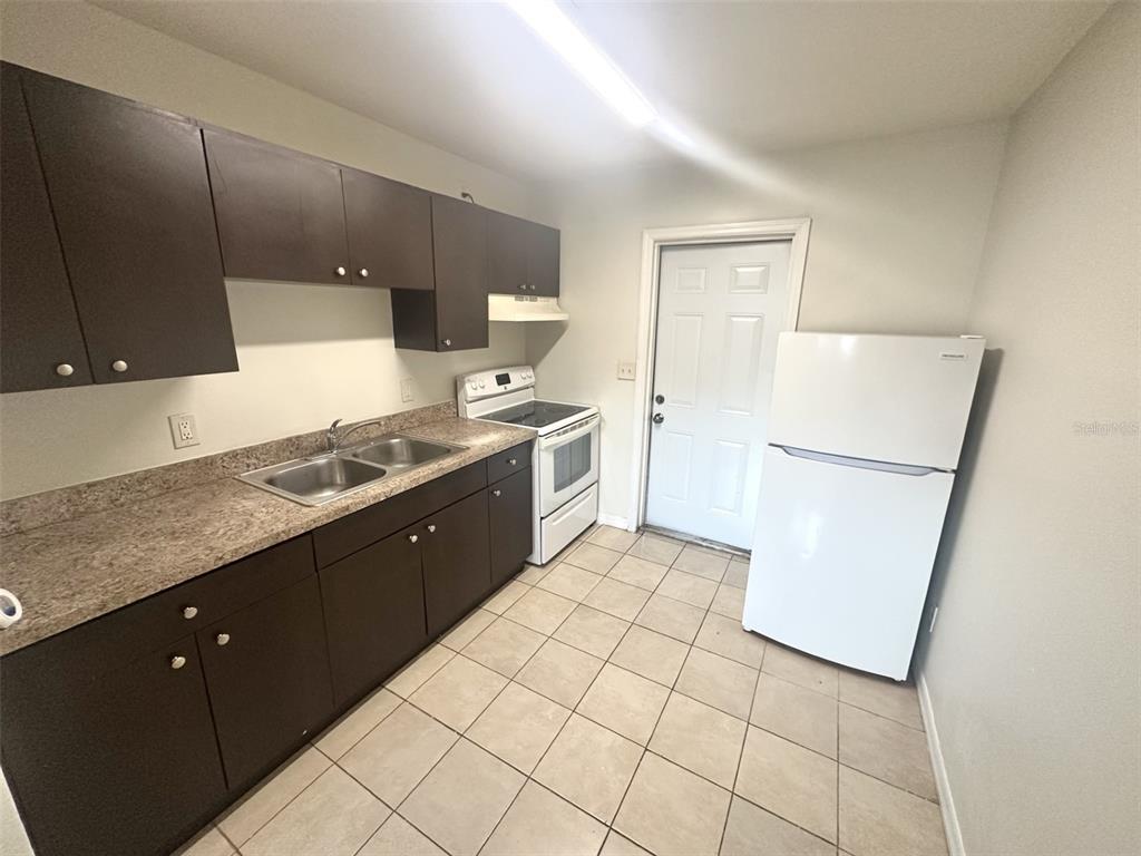A kitchen features dark brown cabinets, a white stove, a white refrigerator, and tiled flooring — 9601 N 10TH STREET UNIT B, TAMPA, FL