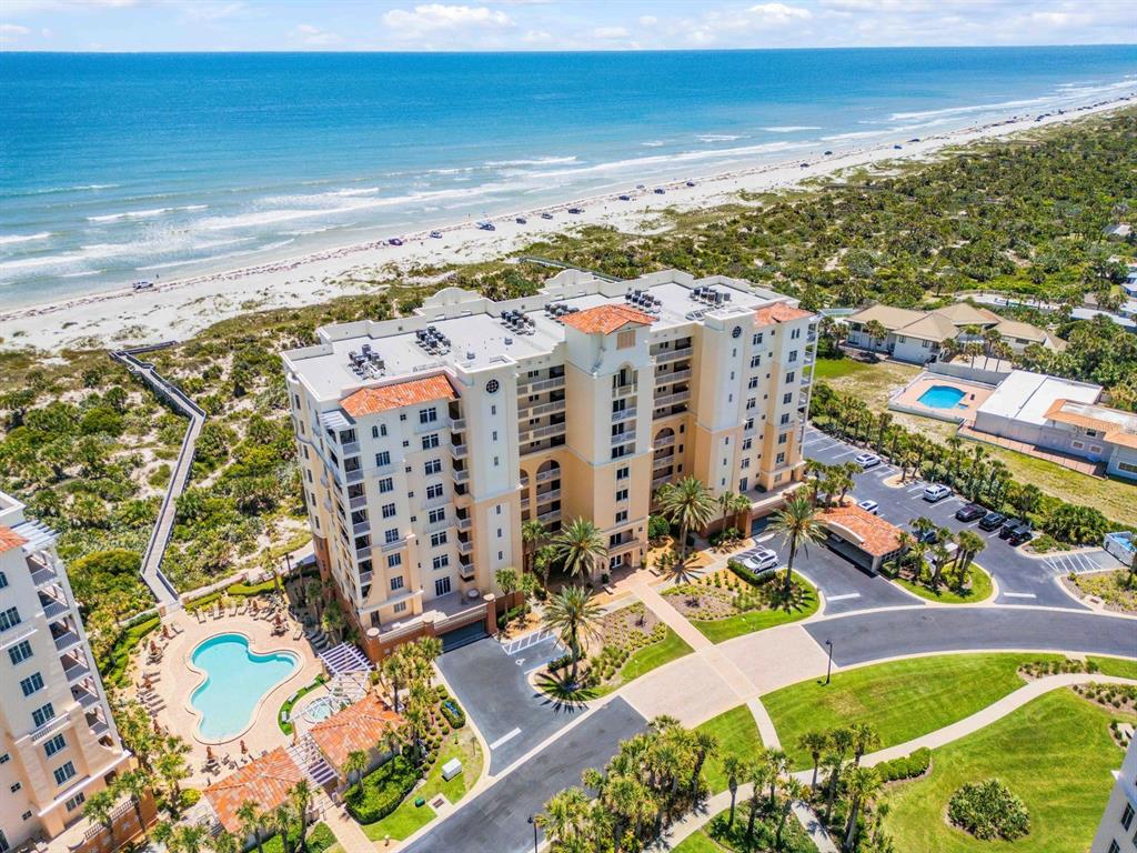 An aerial view shows a multi-story beachfront condominium complex with a pool and parking lot — 253 MINORCA BEACH WAY UNIT 604, NEW SMYRNA BEACH, FL