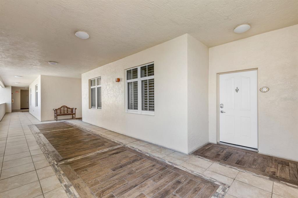 An outdoor hallway features tiled flooring with wood-look inlays, a white door, and a bench — 253 MINORCA BEACH WAY UNIT 604, NEW SMYRNA BEACH, FL