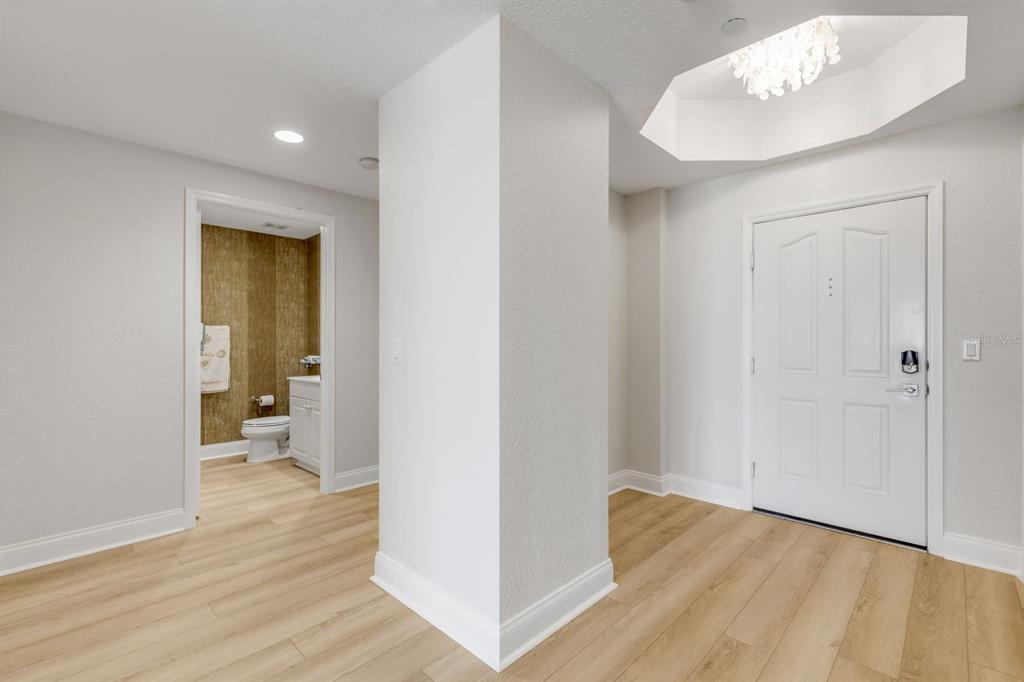 A bright entryway features light wood-look flooring, a white front door, and an adjacent bathroom — 253 MINORCA BEACH WAY UNIT 604, NEW SMYRNA BEACH, FL