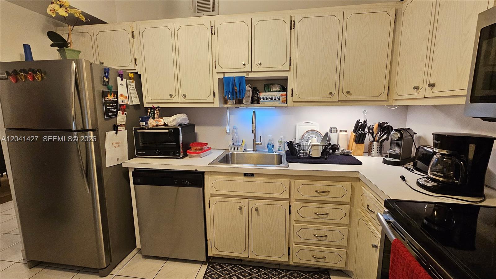 A kitchen features light-colored cabinets, stainless steel appliances, and a tiled floor — 1980 S Ocean Dr # 6B, Hallandale Beach FL 33009, HALLANDALE BEACH, FL