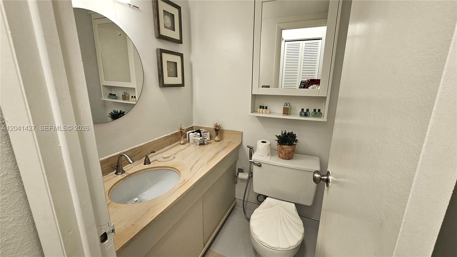 A bathroom features a vanity with a light wood countertop, a toilet, and two mirrors — 1980 S Ocean Dr # 6B, Hallandale Beach FL 33009, HALLANDALE BEACH, FL