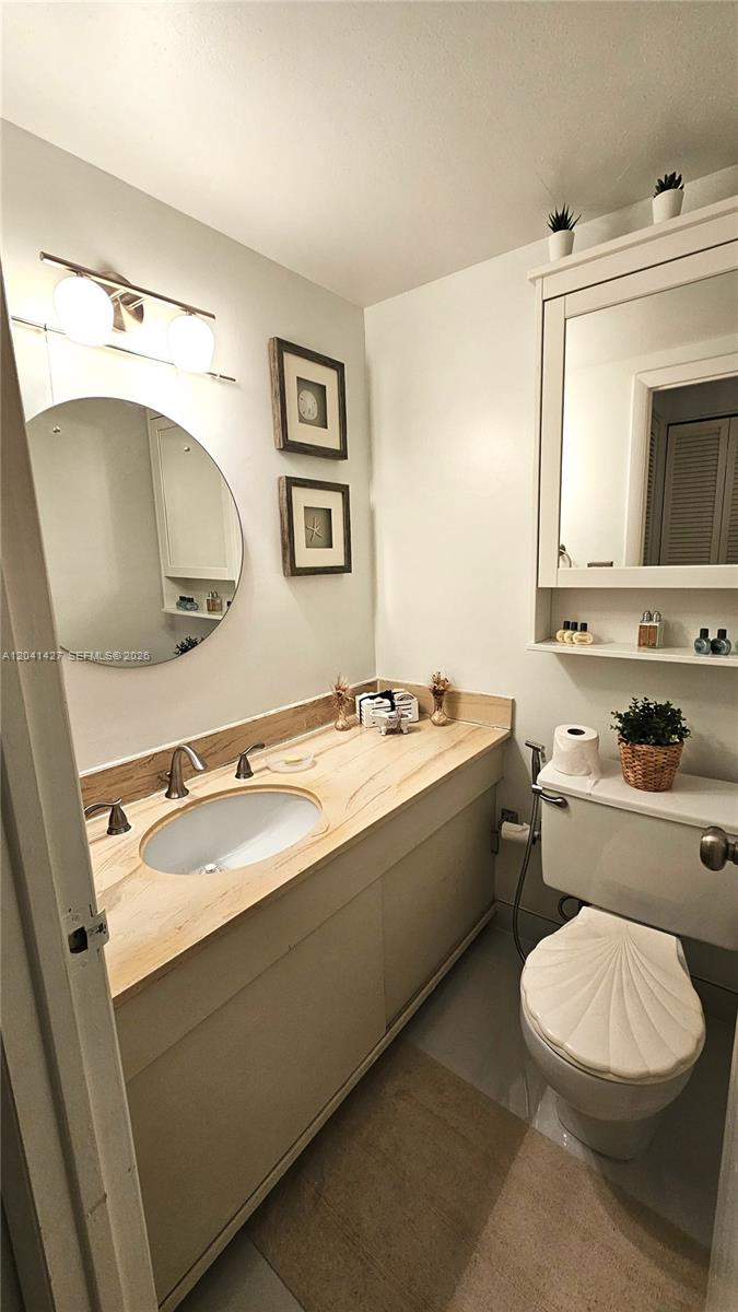 A bathroom features a light wood vanity, a round mirror, and a shell-shaped toilet lid — 1980 S Ocean Dr # 6B, Hallandale Beach FL 33009, HALLANDALE BEACH, FL