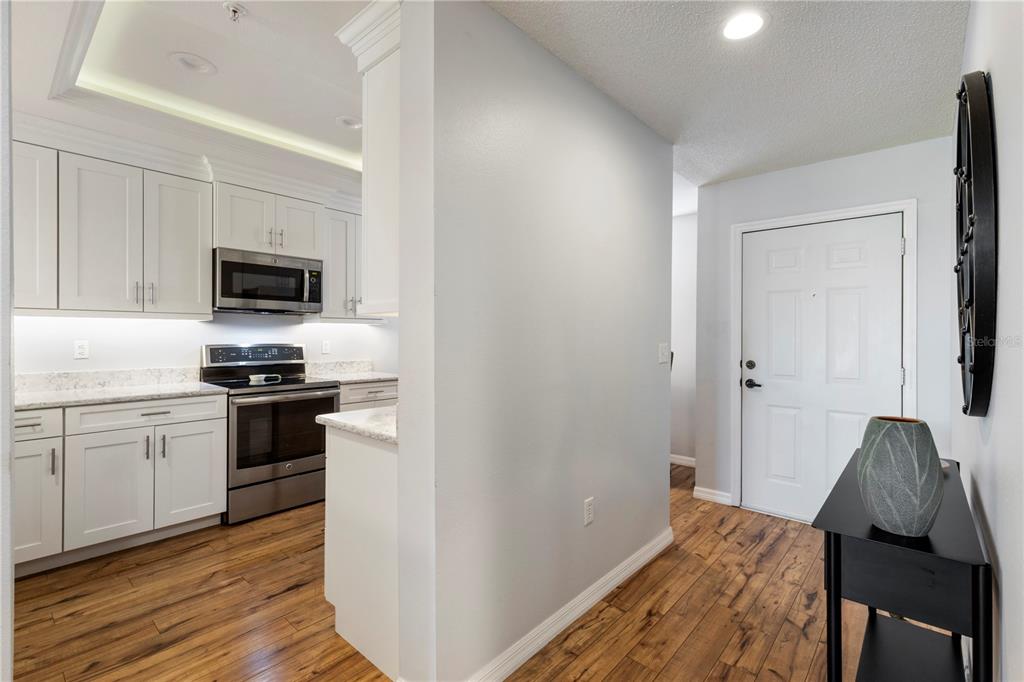 A kitchen with white cabinets and stainless steel appliances sits beside an entryway with wood flooring — 8750 OLDE HICKORY AVENUE UNIT 9103, SARASOTA, FL