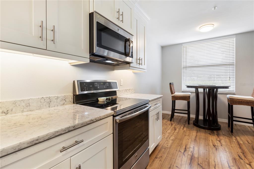 A kitchen features white cabinets, stainless steel appliances, marble-look countertops, and a small dining area — 8750 OLDE HICKORY AVENUE UNIT 9103, SARASOTA, FL