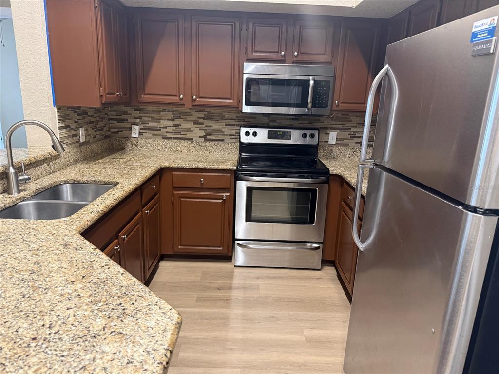 A kitchen features brown cabinets, granite countertops, stainless steel appliances, and a tiled backsplash — 13028 PLANTATION PARK CIRCLE UNIT 1225, ORLANDO, FL