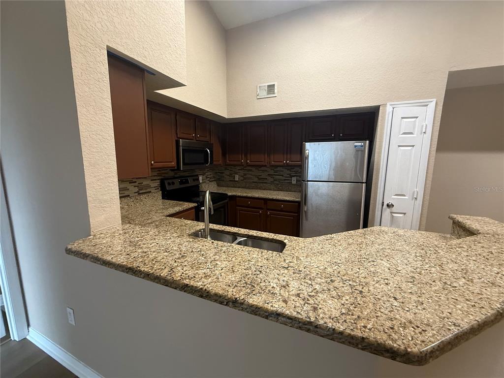 A kitchen features dark wood cabinets, granite countertops, stainless steel appliances, and a breakfast bar — 13028 PLANTATION PARK CIRCLE UNIT 1225, ORLANDO, FL