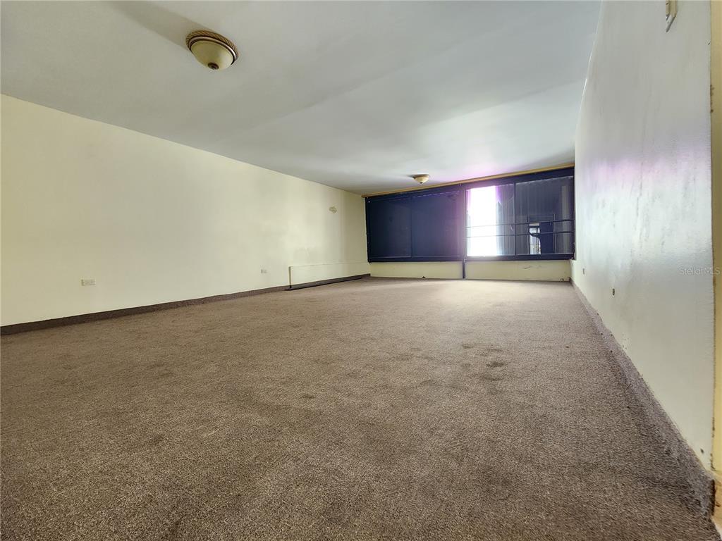 An empty room features beige carpet, plain walls, and a large window with dark shades — Condado 8-18 C-MANUEL RODRIGUEZ SERRA UNIT 7B, SAN JUAN, PR
