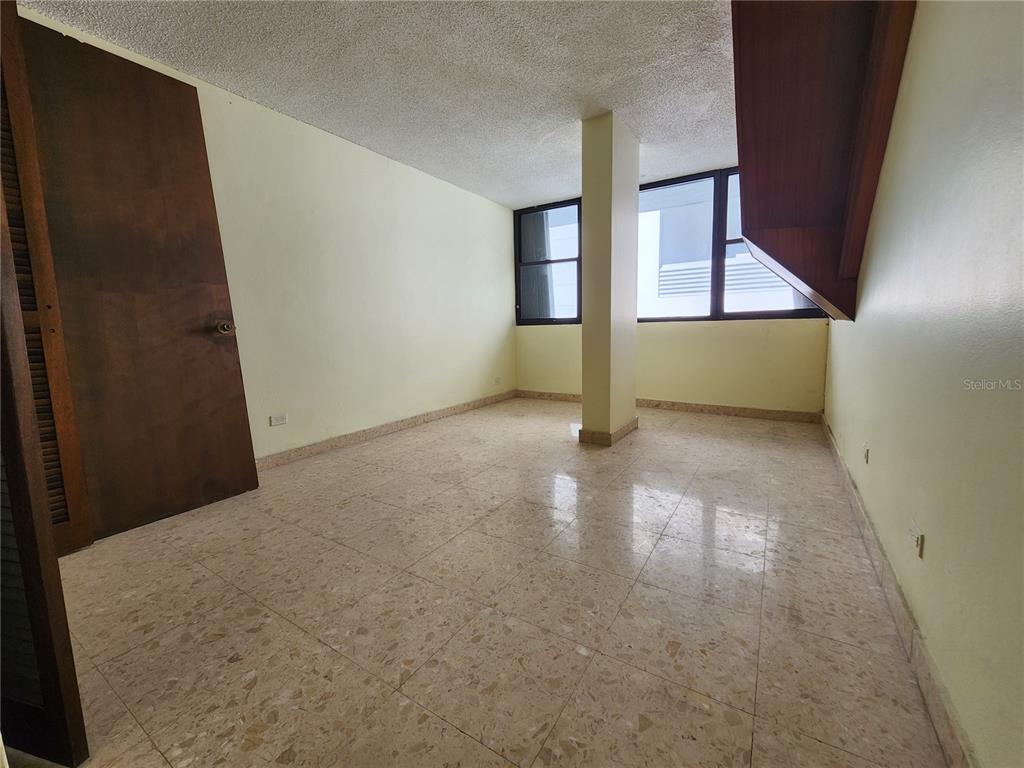 An empty room features light-colored tile flooring, pale yellow walls, and a central support column — Condado 8-18 C-MANUEL RODRIGUEZ SERRA UNIT 7B, SAN JUAN, PR