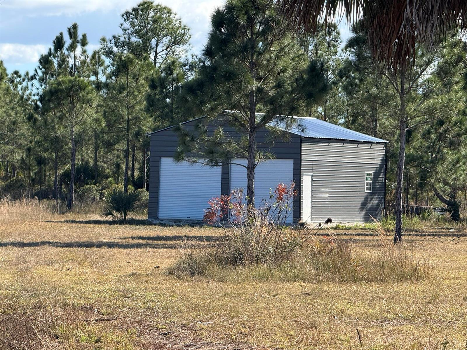 A detached metal garage with two roll-up doors and a side entry door sits outdoors — 16382 NW 286th Street, Okeechobee FL 34972, OKEECHOBEE, FL
