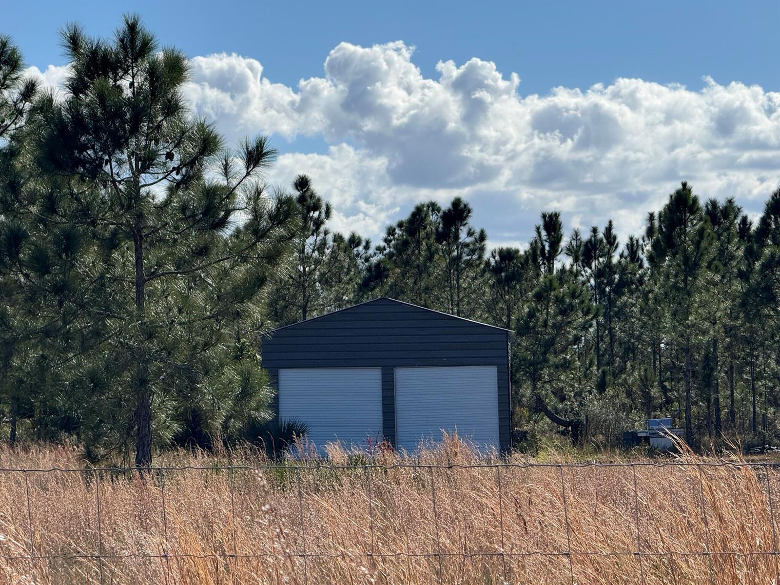 A dark gray metal garage with two roll-up doors sits in a grassy field — 16382 NW 286th Street, Okeechobee FL 34972, OKEECHOBEE, FL