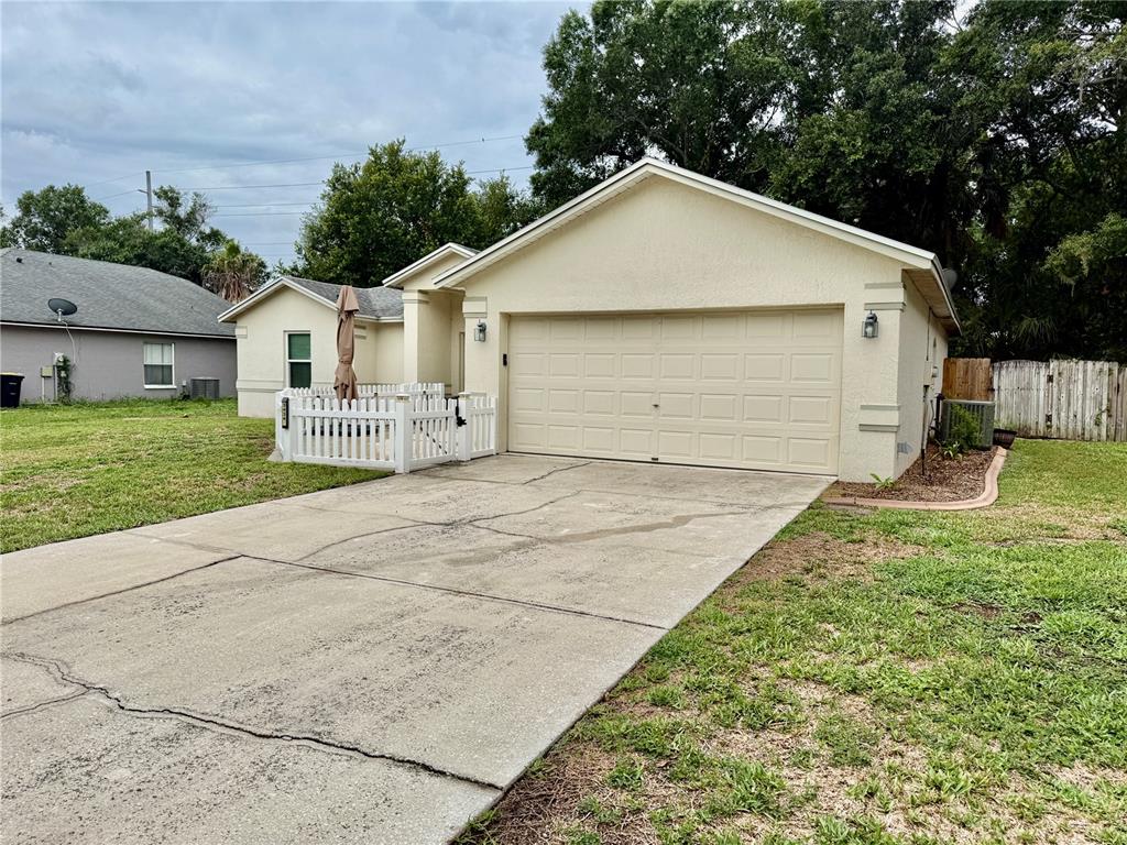 A beige single-story house with a two-car garage and a small white picket fence — 3434 DIAMOND TERRACE, MULBERRY, FL